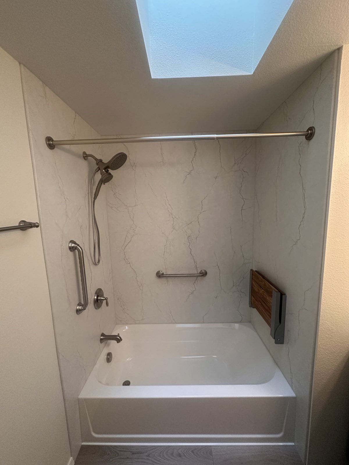 Accessible bath with marble-look surround, skylight, and teak fold-down seat