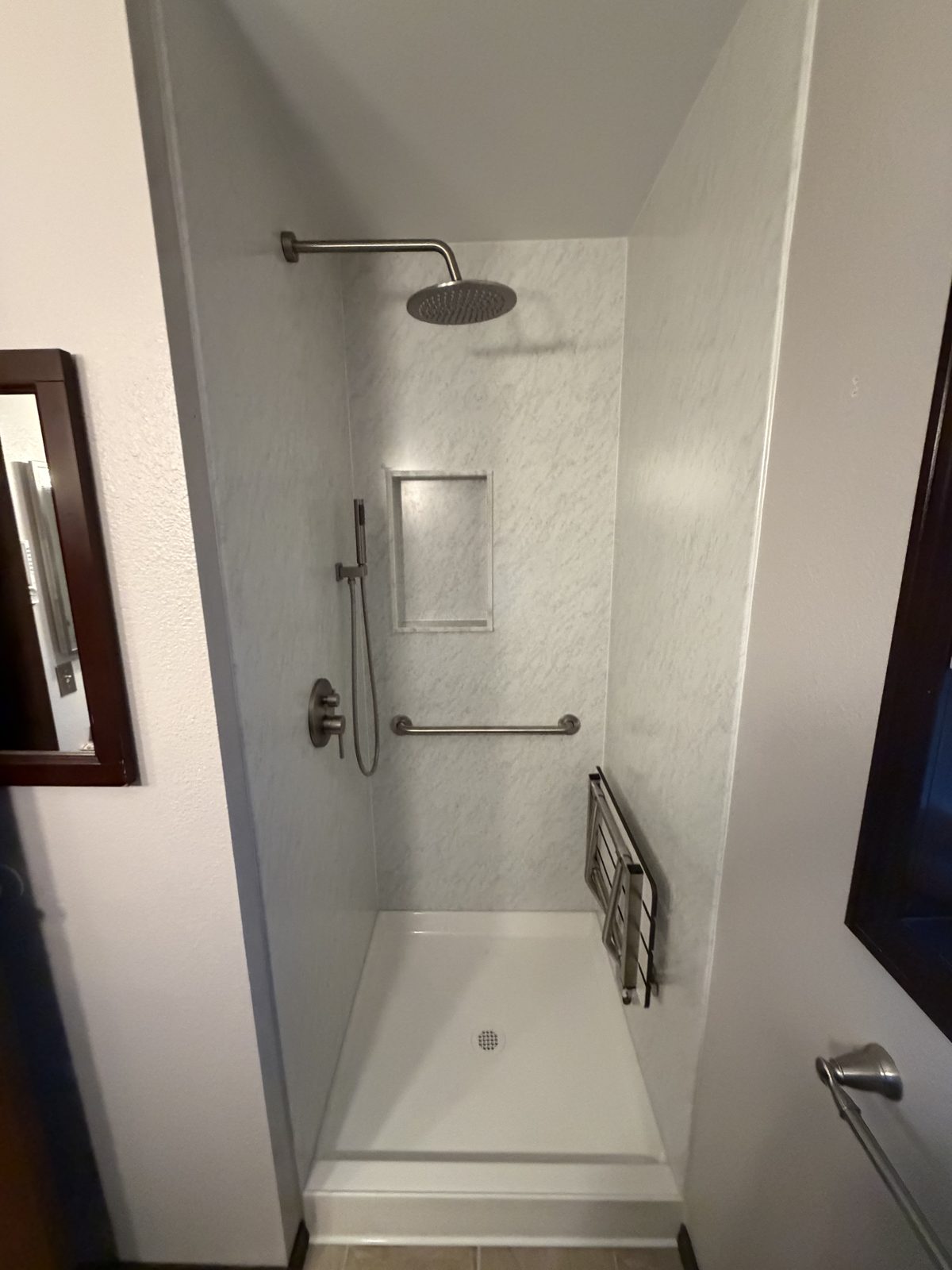 Accessible walk-in shower with rain head, niche, grab bar, and fold-up seat