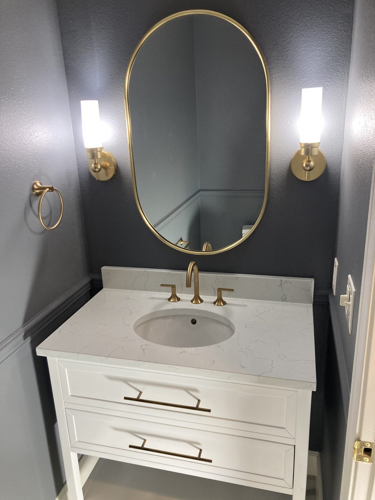Powder-room remodel with navy walls, brass fixtures, and quartz-top vanity